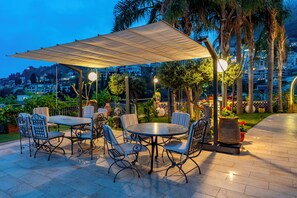 An outdoor seating area with tables and chairs, a canopy, and a view of a cityscape. - Oikos Taormina - Apartment with pool and garden (Taormina)