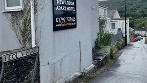 Un immeuble portant une enseigne indiquant « KG Short Stay New Lodge Apart Hotel », avec un numéro de téléphone et une adresse de site web.