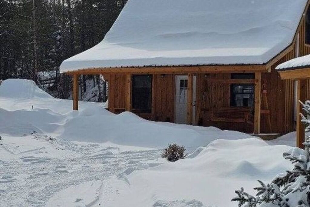 En stuga av trä med ett snötäckt tak, omgiven av snö.