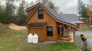 En stuga av trä med ett sluttande tak, en veranda och två stora vita containrar framför.