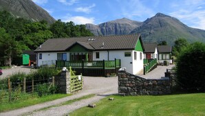 A two-story building with a green and white exterior, a gravel driveway, and a stone wall.