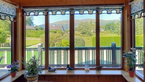 A wooden room with a view of a green landscape, a balcony with a railing, and decorative items on the windowsill.