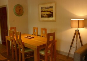 Uma área de refeições com mesa e cadeiras de madeira, um relógio, um quadro emoldurado e um abajur.