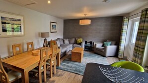 A modern living room with a dining table, sofas, and a large window with curtains.