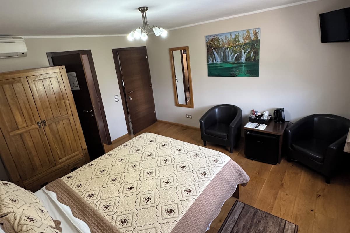A bedroom with a bed, two chairs, a TV, a painting, and a wardrobe.