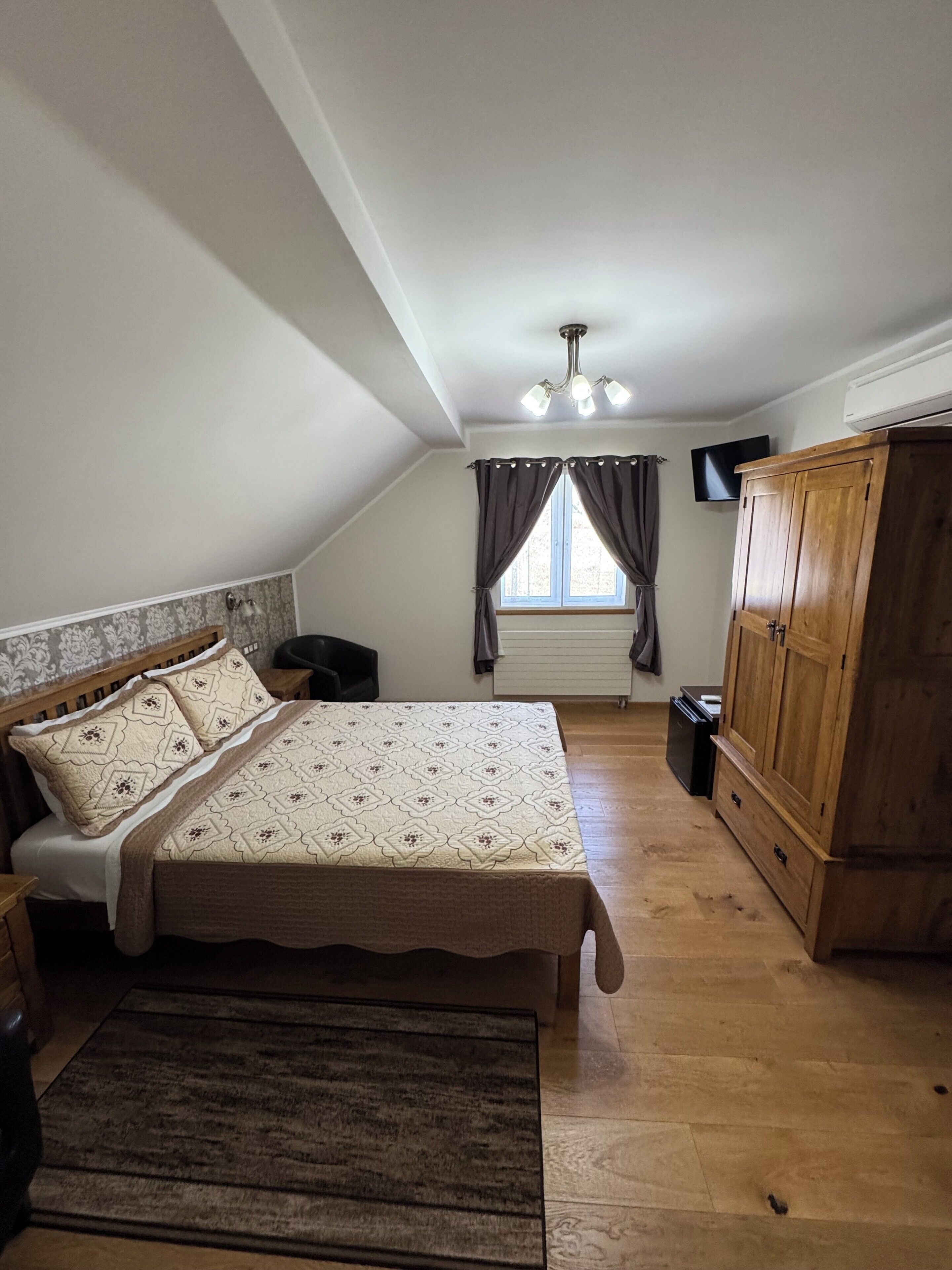 A bedroom with a bed, wooden wardrobe, and a window with curtains.