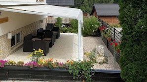 A house with a covered patio, outdoor seating, and a garden with flowers.