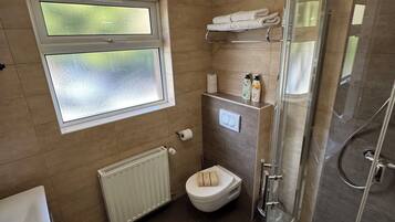 A modern bathroom with a glass shower enclosure, a toilet, a sink, and a window with frosted glass.
