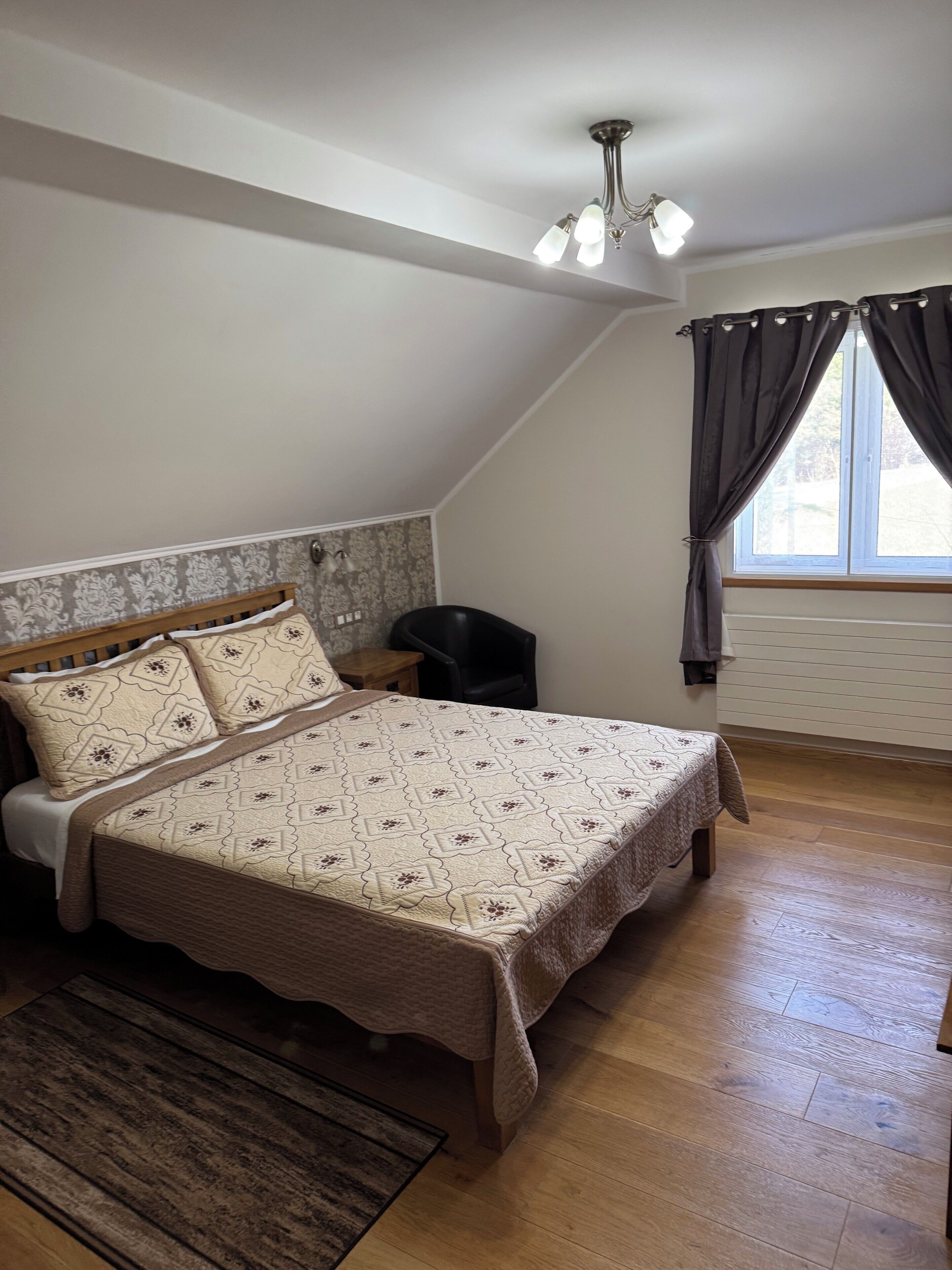 A bedroom with a bed, a wooden floor, a ceiling light fixture, and a window with curtains.