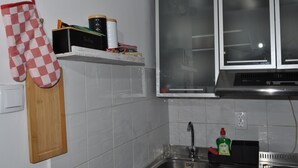 Een keuken met een houten snijplank, een ovenwant met rode en witte ruitjes, een roestvrijstalen spoelbak en een raam met geëtste glas.