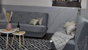Een woonkamer met een grijze bank, een klein rond tafeltje en een tapijt met een patroon.