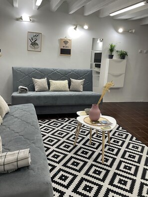 A modern living room with a grey sofa, a patterned rug, a small round table with a vase, and a wall-mounted TV. - Tip Top downtown (Podgorica)