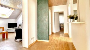 A spacious hallway with a high ceiling, a large window, a flat-screen TV, and a desk with a chair.