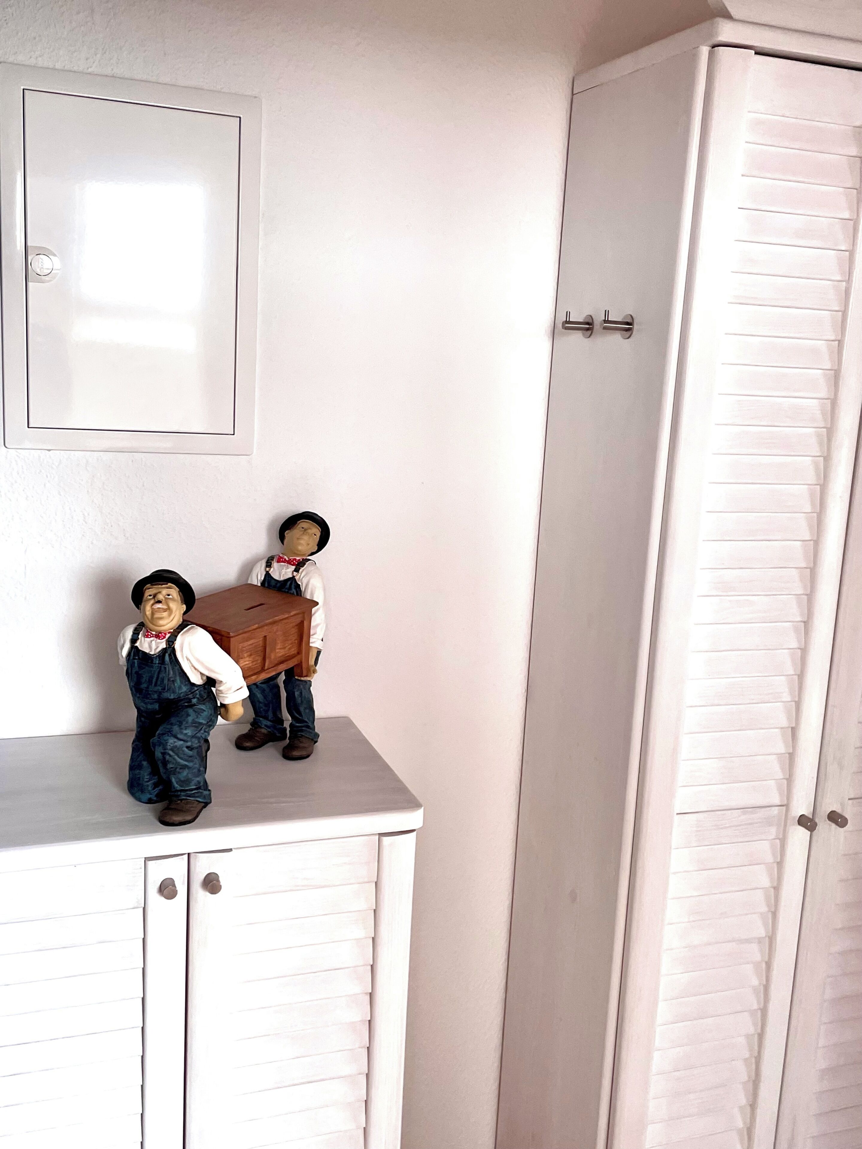 A white wardrobe with a mirror above it and two figurines on a shelf.