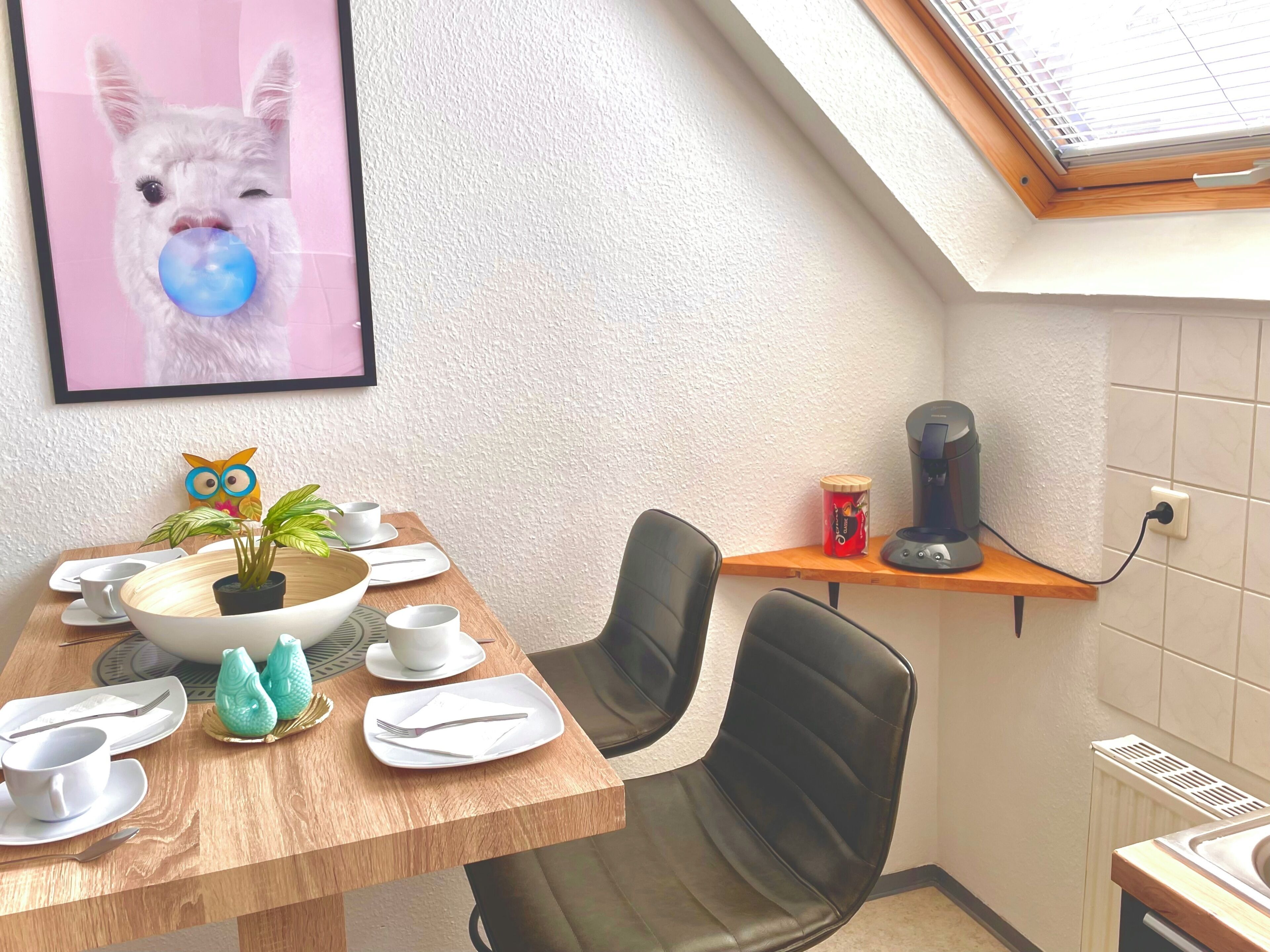 A dining area with a wooden table, chairs, a coffee machine, and a small shelf with a kettle.