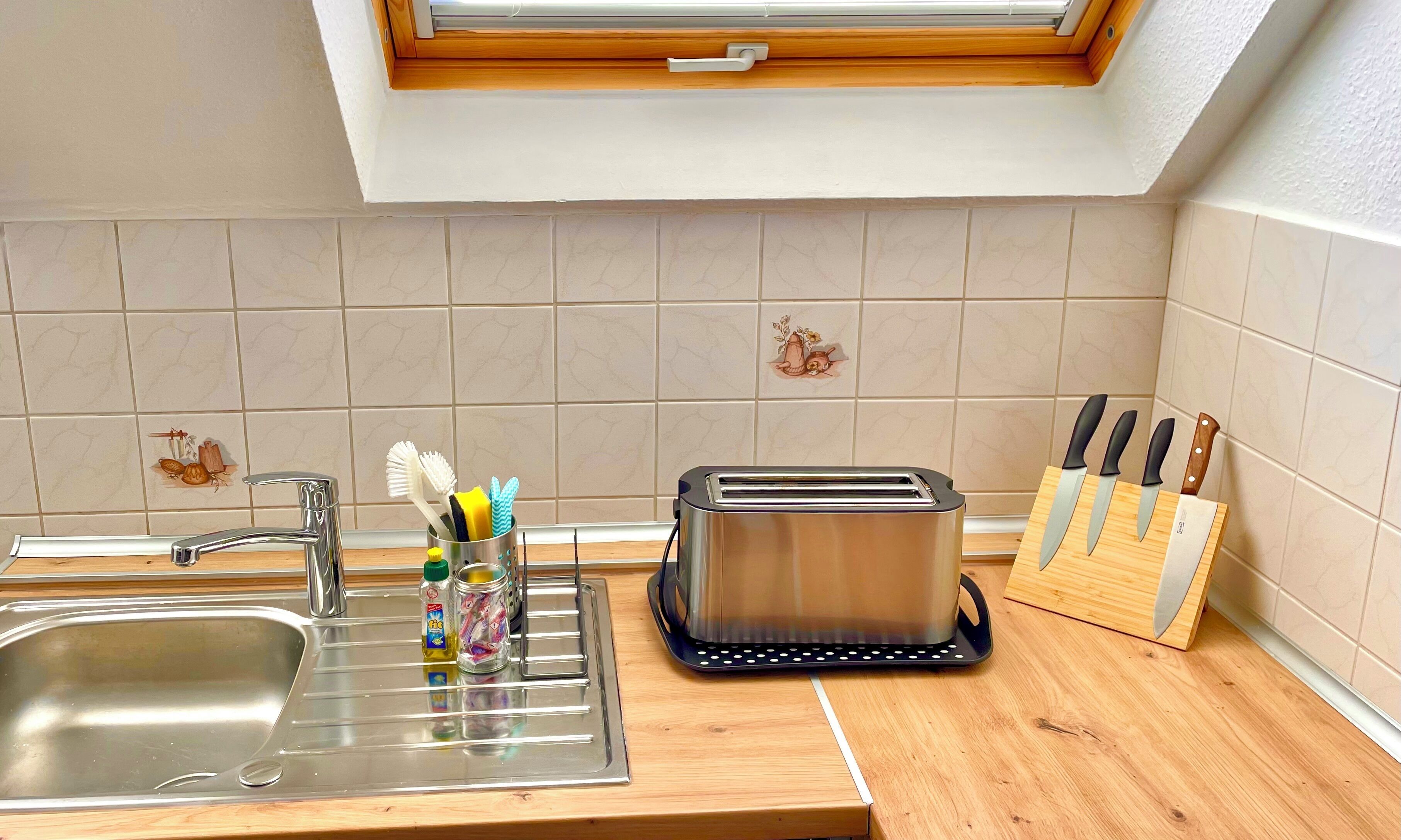 Una cocina con un lavamanos, un tostador y un juego de cuchillos.