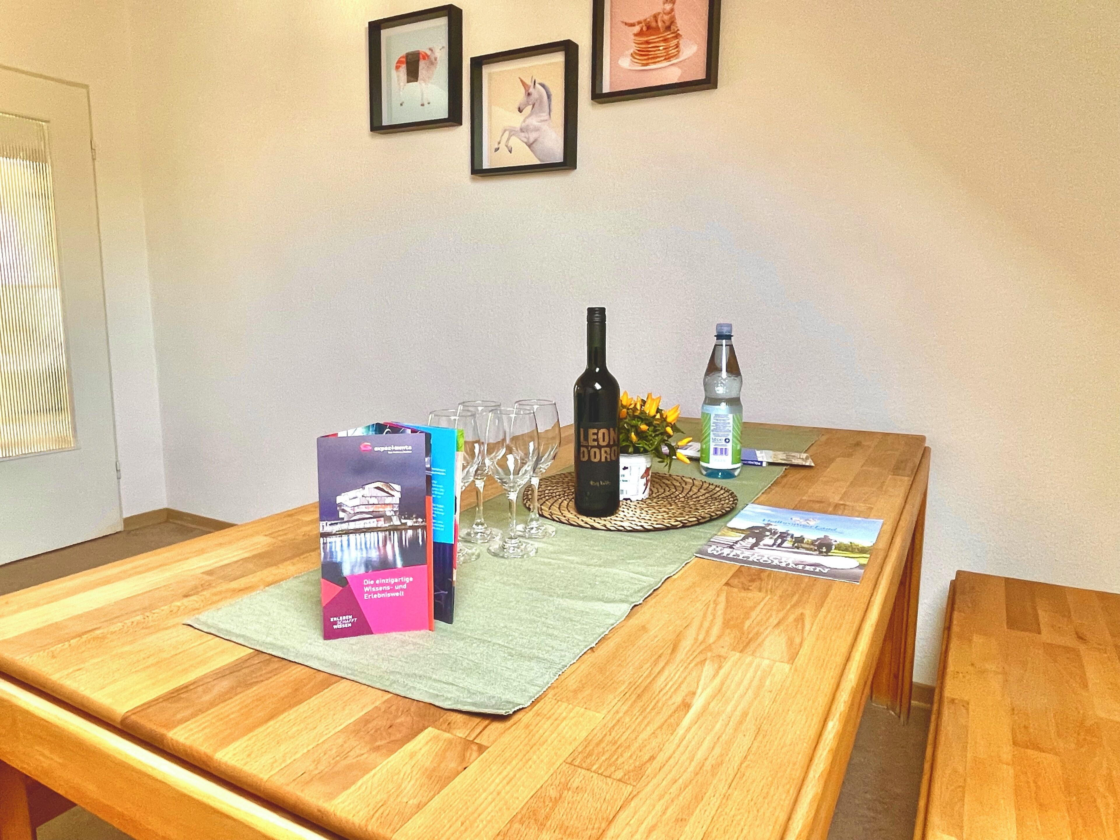 A wooden table with a placemat, wine bottle, glasses, a water bottle, and brochures.