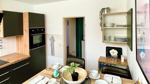 A modern kitchen with a dining area, wooden cabinets, a built-in oven, and a dining table set with plates, cups, and a potted plant.