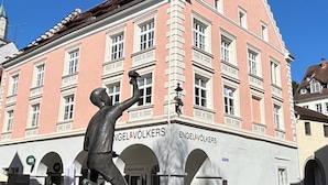 A pink building with 'Engel & Volkers' signage, a statue, and a car parked in front. - LAKE Loft Leaf - Pflummernhaus (Überlingen)