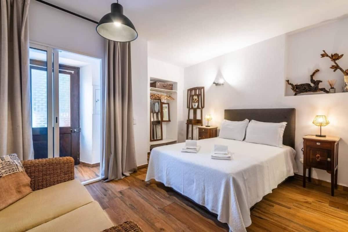 A bedroom with a bed, bedside tables, a lamp, a wardrobe, a mirror, and a door leading to a balcony.