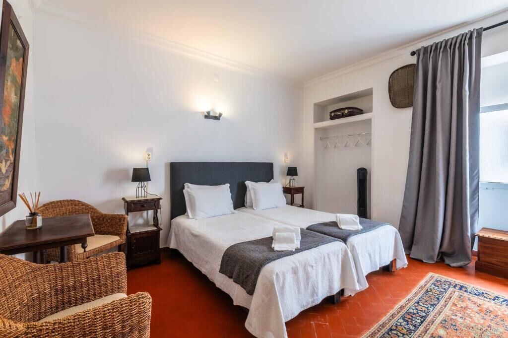 Une chambre d’hôtel avec deux lits, une table à manger, des meubles en osier, un tapis et une étagère fixée au mur.