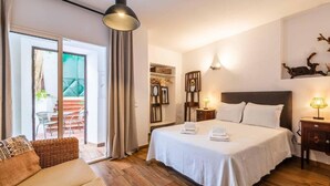 Een hotelkamer met een bed, een bank, een eethoek met een tafel en stoelen, en een glazen schuifdeur naar een buitenruimte.