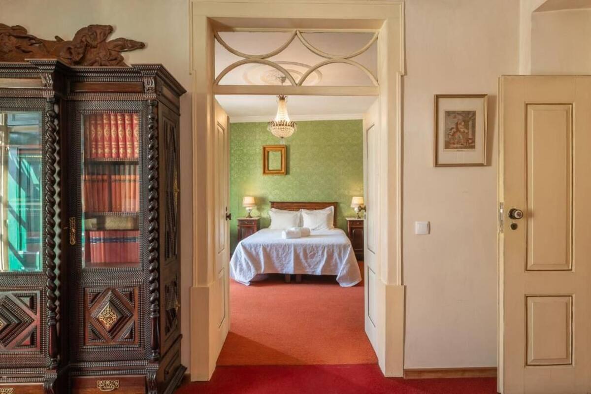 A hotel room with a bed, a chandelier, a green wall, and a wooden cabinet.