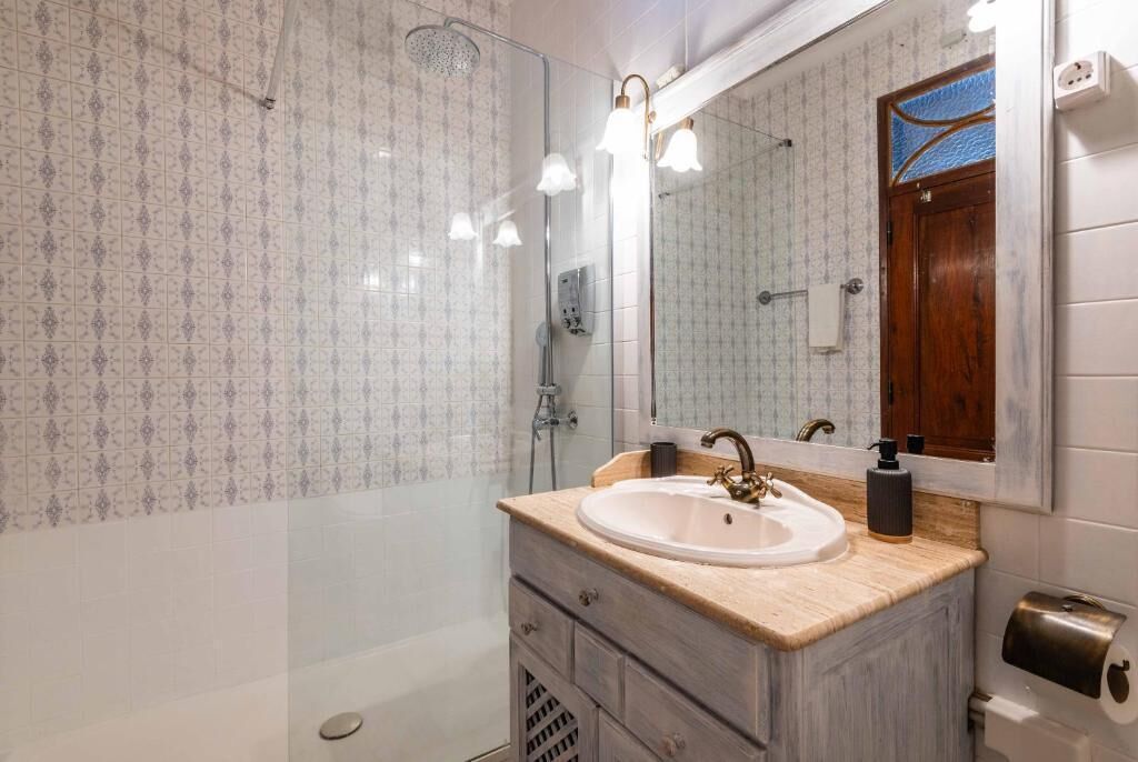 Een badkamer met een wastafel, spiegel, douche en handdoekdispenser.