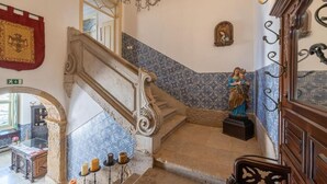 Een trap met versierde balustrades, een standbeeld en een kroonluchter.