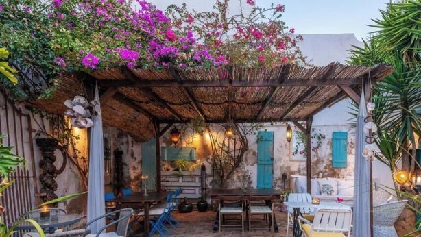 Een rustieke buitenruimte met een pergola, houten tafels en stoelen.
