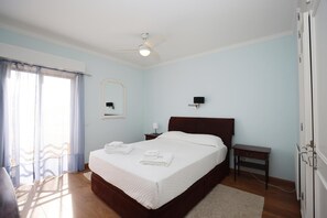 Ein Schlafzimmer mit Bett, Nachttisch, Spiegel, Deckenventilator und einer Tür.