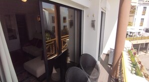 Ein Balkon mit einer Couch und zwei Stühlen, eine Schiebeglastür und Blick auf ein Gebäude mit Balkonen.