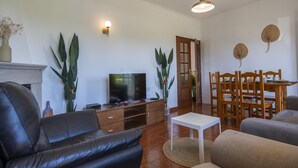 A living room with a leather sofa, a TV, a dining table with chairs, and a fireplace. - U 01 - Bedroom 1 in Casa Quinta Estação (Lagos)
