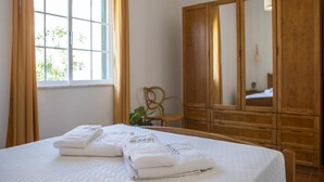 A hotel room with a bed, a wooden wardrobe, a chair, and a window with curtains. - U 01 - Bedroom 1 in Casa Quinta Estação (Lagos)