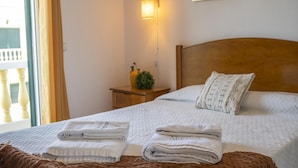 A neatly made bed with folded towels, a wooden headboard, a bedside table with a plant, and a wall-mounted lamp.