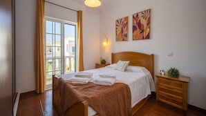 A bedroom with a bed, a nightstand, a lamp, a window with curtains, and two wall art pieces.