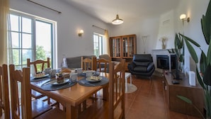 A dining area with a wooden table, chairs, and a buffet setup. There is a fireplace and a large window with curtains.