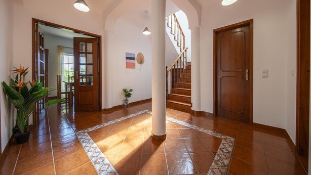 A spacious hallway with a tiled floor, a staircase, and a wooden door.
