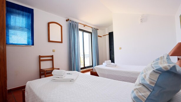 A hotel room with two beds, a wooden chair, a window with curtains, and a wall-mounted mirror. - B46 - Belavista Torraltinha Flat (Lagos)