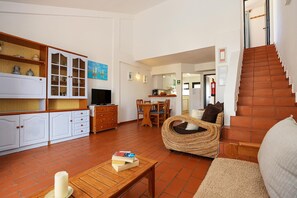 A living room with a sofa, a wicker chair, a TV, and a dining area with chairs and a table. - B46 - Belavista Torraltinha Flat (Lagos)