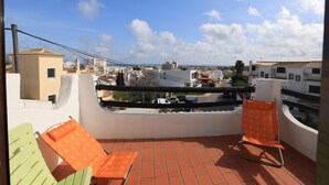 Un balcon avec deux chaises, une vue sur une ville côtière et un ciel dégagé.