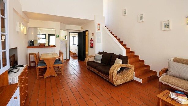 Un salon avec un canapé, une table à manger avec des chaises, un escalier et un coin cuisine.