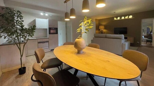 Een moderne eetruimte met een ronde houten tafel, zwarte stoelen, hangende lampen en een potplant.