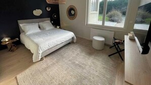 Quarto com cama, janela, radiador, um banquinho pequeno e televisão.