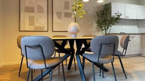 Uma área de refeições moderna com uma mesa redonda, quatro cadeiras cinzentas, luminárias pendentes e arte abstrata na parede.