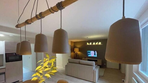 Cozinha moderna com eletrodomésticos embutidos, área de jantar com mesa e cadeiras redondas e sala de estar com sofá e televisão.
