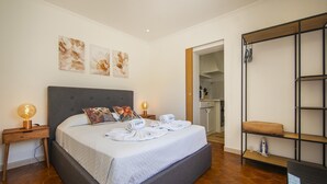 A neatly made bed with a grey headboard, a bedside table with a lamp, and a wall with three floral paintings. - S 01 - 1 Bed Apartment in Quinta Silvestre (Lagos)
