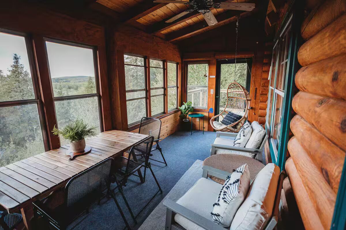 A log cabin interior with a dining table, chairs, a sofa, and a hanging chair.