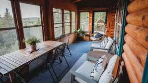 L’intérieur d’une cabane en rondins, avec une table à manger, des chaises, un canapé et un fauteuil suspendu.