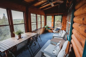 Interior de una cabaña de troncos con una mesa de comedor, sillas, un sofá y un sillón colgante.